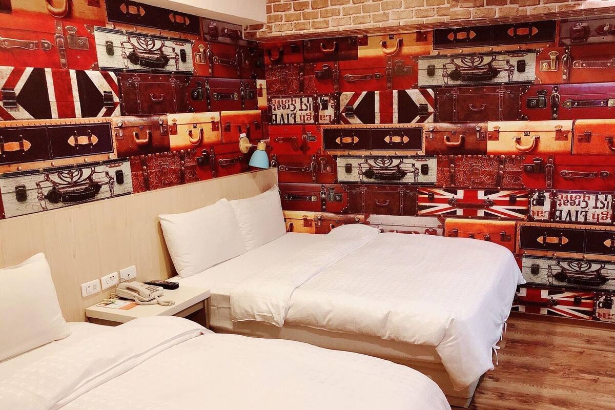 A hotel room with two beds, a brick wall, and a wall of suitcases.