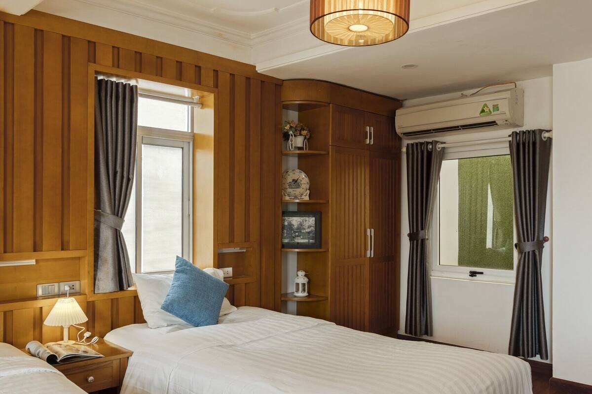 Une chambre d’hôtel avec deux lits, des lambris en bois, un luminaire au plafond, un appareil de climatisation et une fenêtre avec des rideaux.