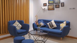 Een moderne woonkamer met een blauwe zithoek, een glazen salontafel en een houten lambrisering.