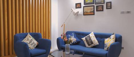 A modern living room with a blue sofa set, a glass coffee table, and a wooden slatted wall.