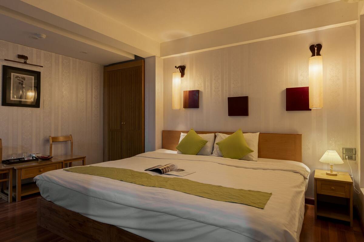 Une chambre d’hôtel avec un grand lit, une tête de lit en bois, des tables de chevet, un bureau et une chaise.