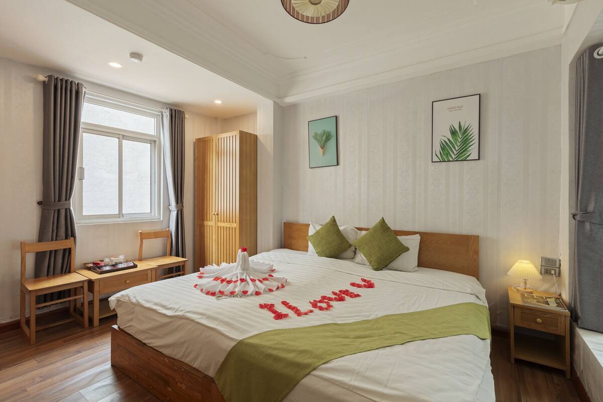 Une chambre d’hôtel avec un lit, un bureau en bois, une chaise, une armoire et une fenêtre.