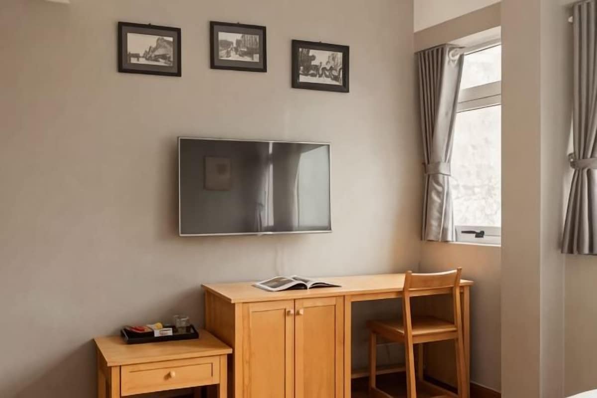Une pièce comprenant un bureau en bois, une chaise, un téléviseur à écran plat fixé au mur et trois tableaux encadrés au-dessus du bureau.