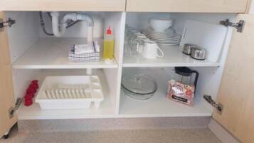 Una cocina con armarios blancos, un lavamanos y diversos utensilios como platos, tazas y una cafetera.