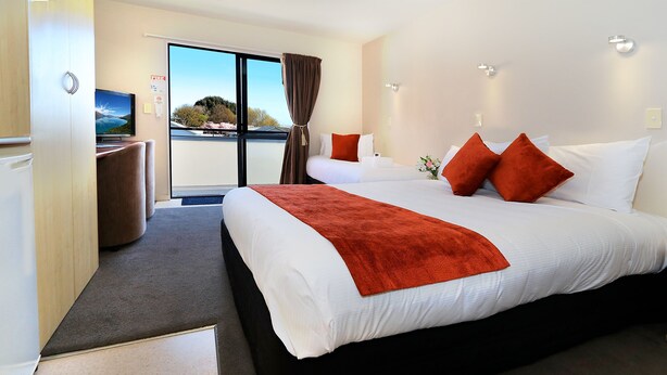 A hotel room with a large bed, a TV, and a view of the outdoors. - Bella Vista Motel Invercargill (Invercargill)