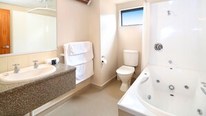A modern bathroom with a granite countertop sink, a white toilet, and a large white bathtub. - Bella Vista Motel Invercargill (Invercargill)