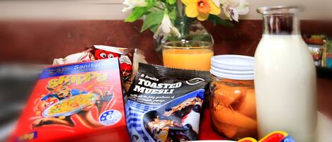 A breakfast setting with a plate of sliced fruit, a glass of orange juice, a bottle of milk, and packaged food items.