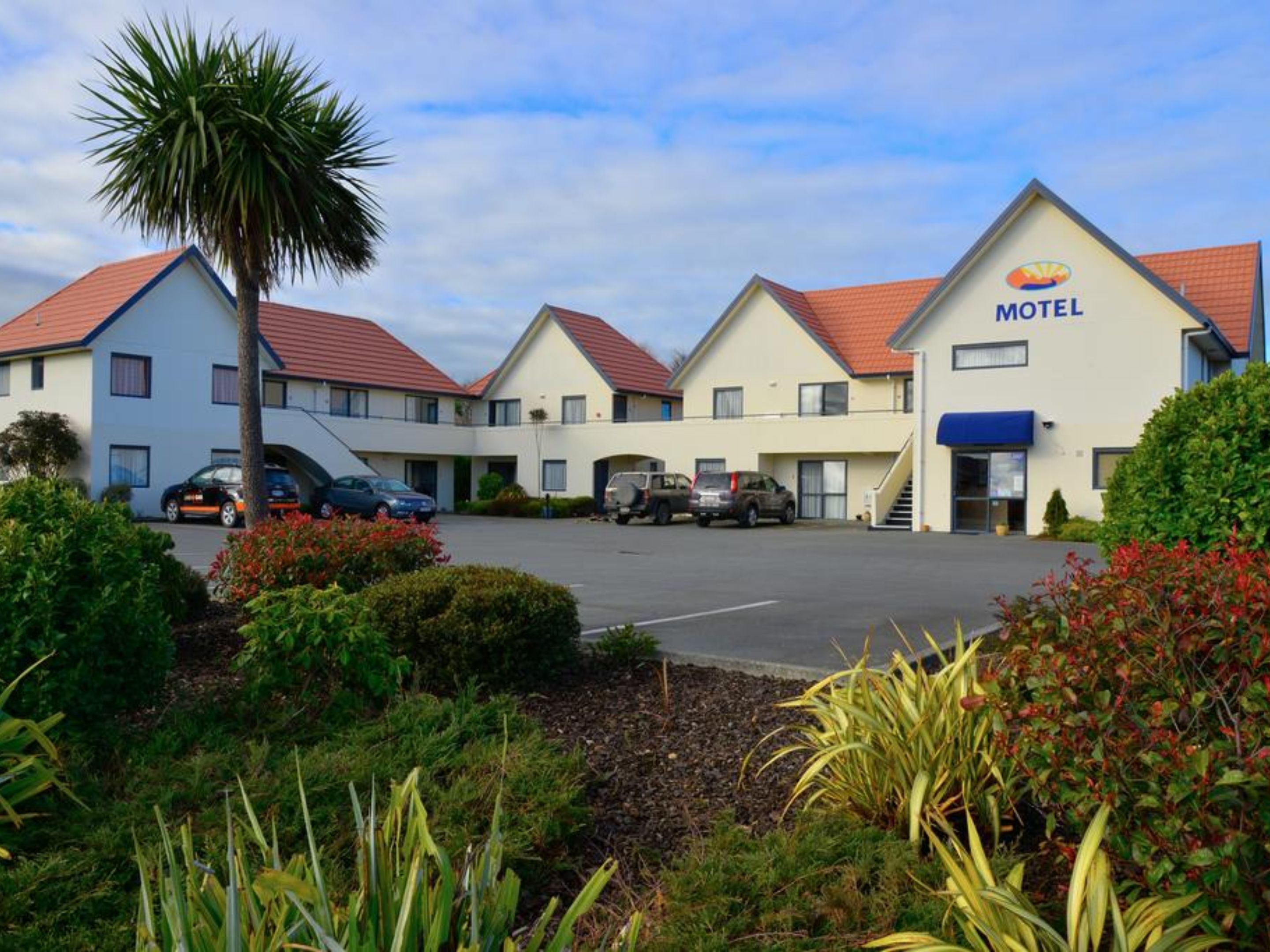 A motel with a two-story building, a parking lot, and a palm tree in the foreground.