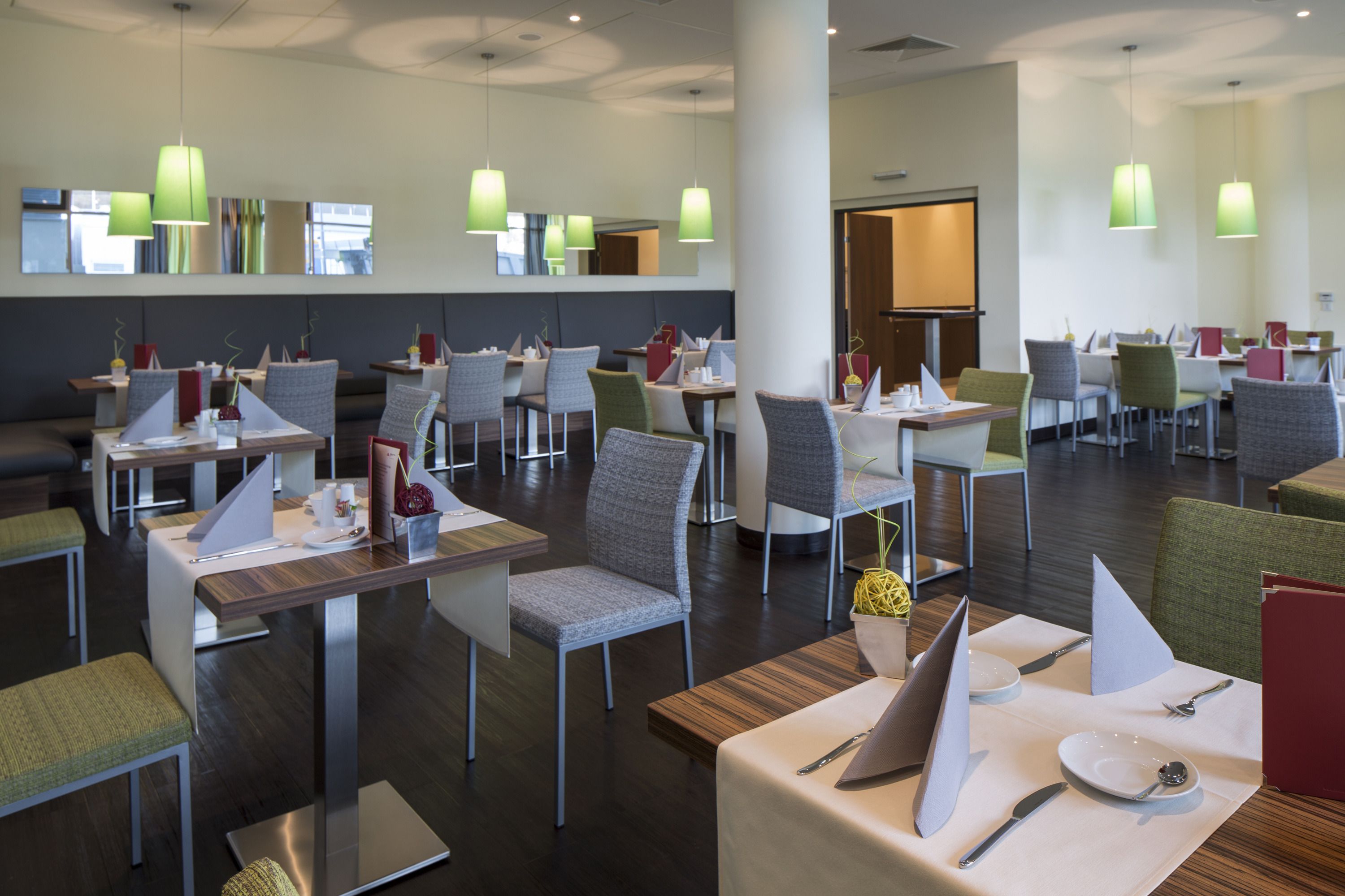 A modern dining area with multiple tables and chairs, green pendant lights, and a neutral color palette.