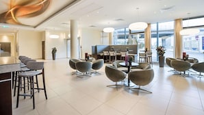 A modern hotel lobby with a bar area, seating arrangements, and large windows. - Austria Trend Hotel Doppio (Vienna)
