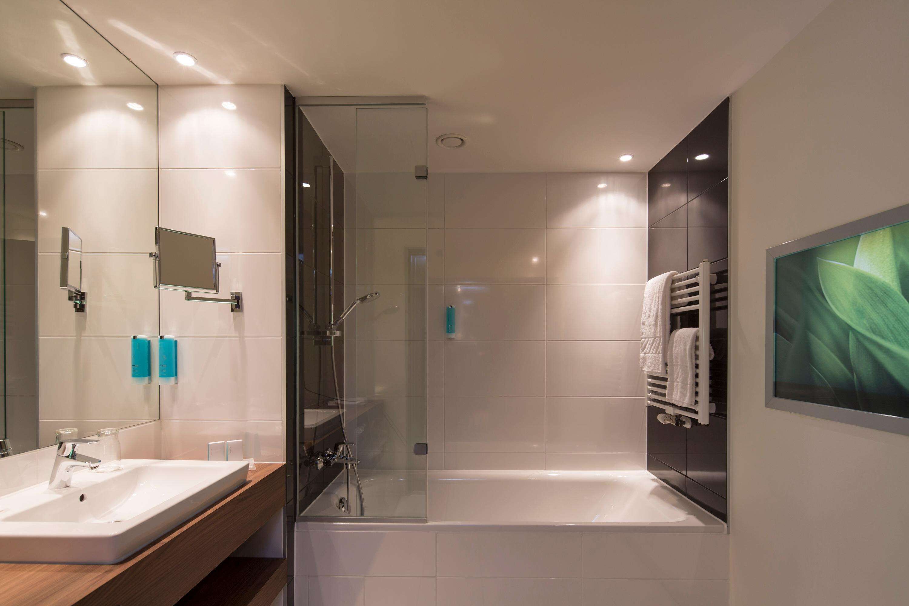 Un baño moderno con ducha acristalada, un espejo grande y una bañera blanca.