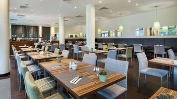 Un restaurante espacioso con varias mesas y sillas, una barra con mostrador y un diseño moderno en el techo.