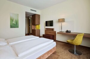 Een hotelkamer met een bed, een bureau met stoel, een televisie en een lamp.