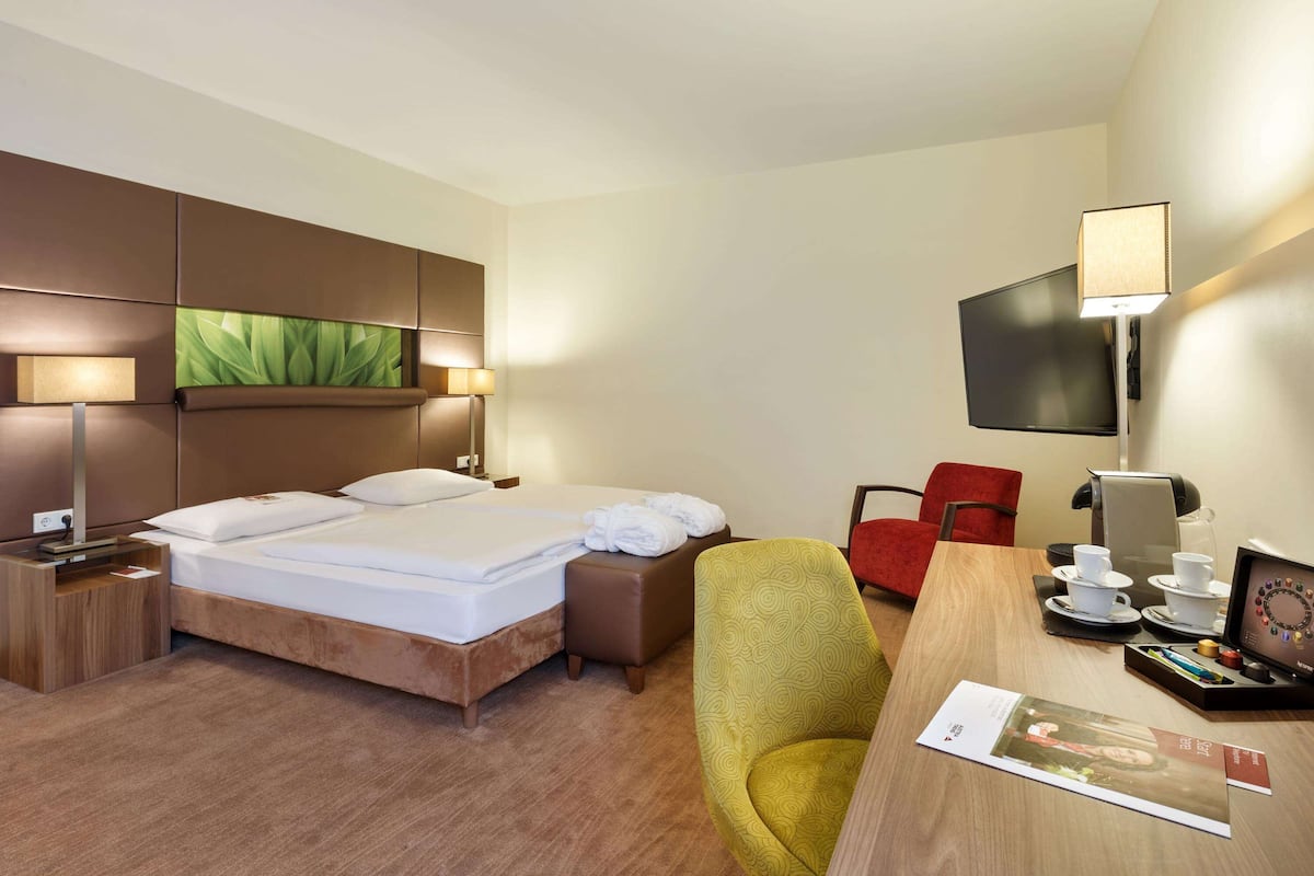 Habitación de hotel con cama, escritorio, computadora, silla, televisor y lámpara.
