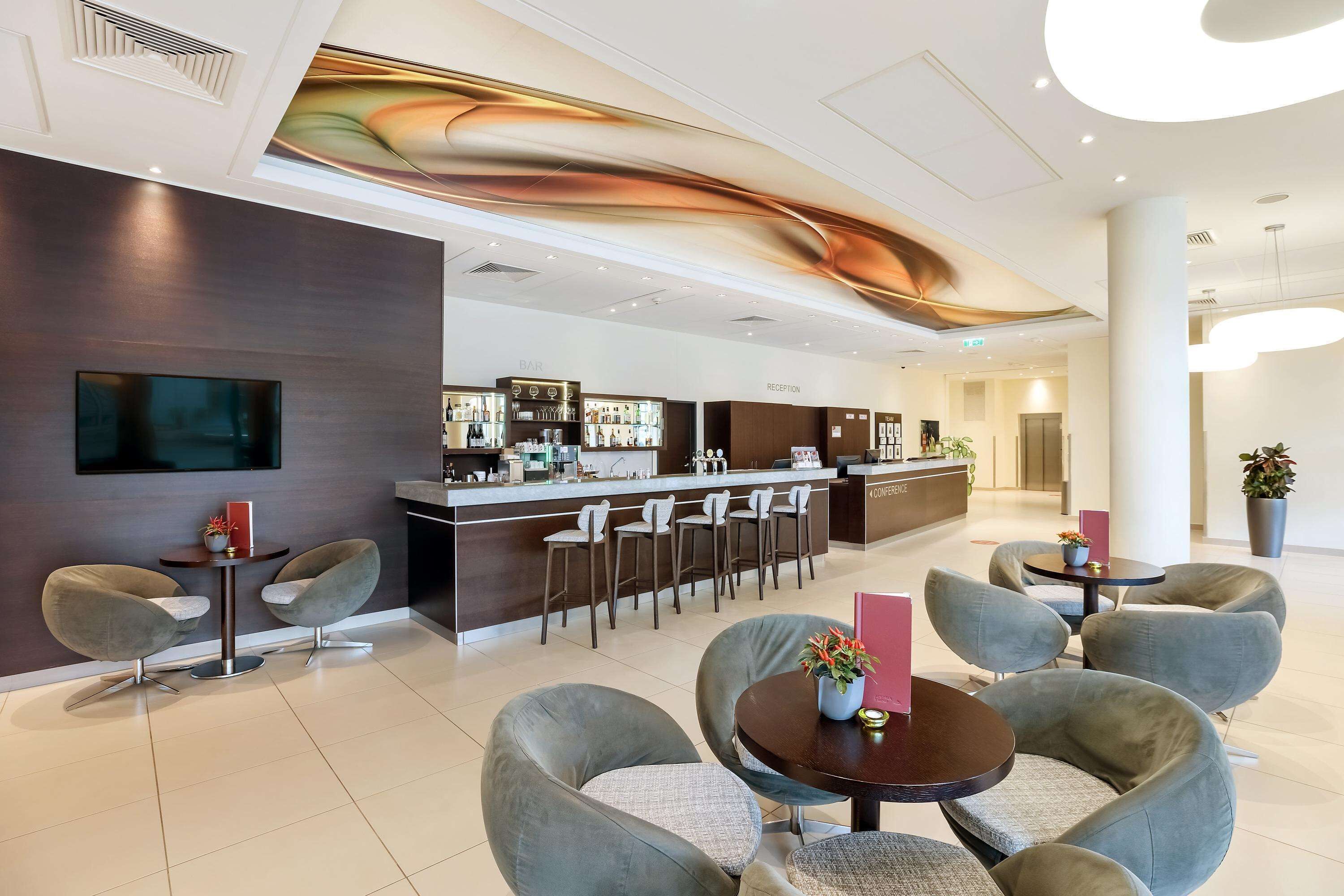 Una hall moderna di un hotel con area bar, posti a sedere e reception.