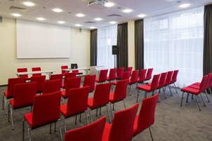 Una sala conferenze con file di sedie rosse, una lavagna e uno schermo per proiettore.