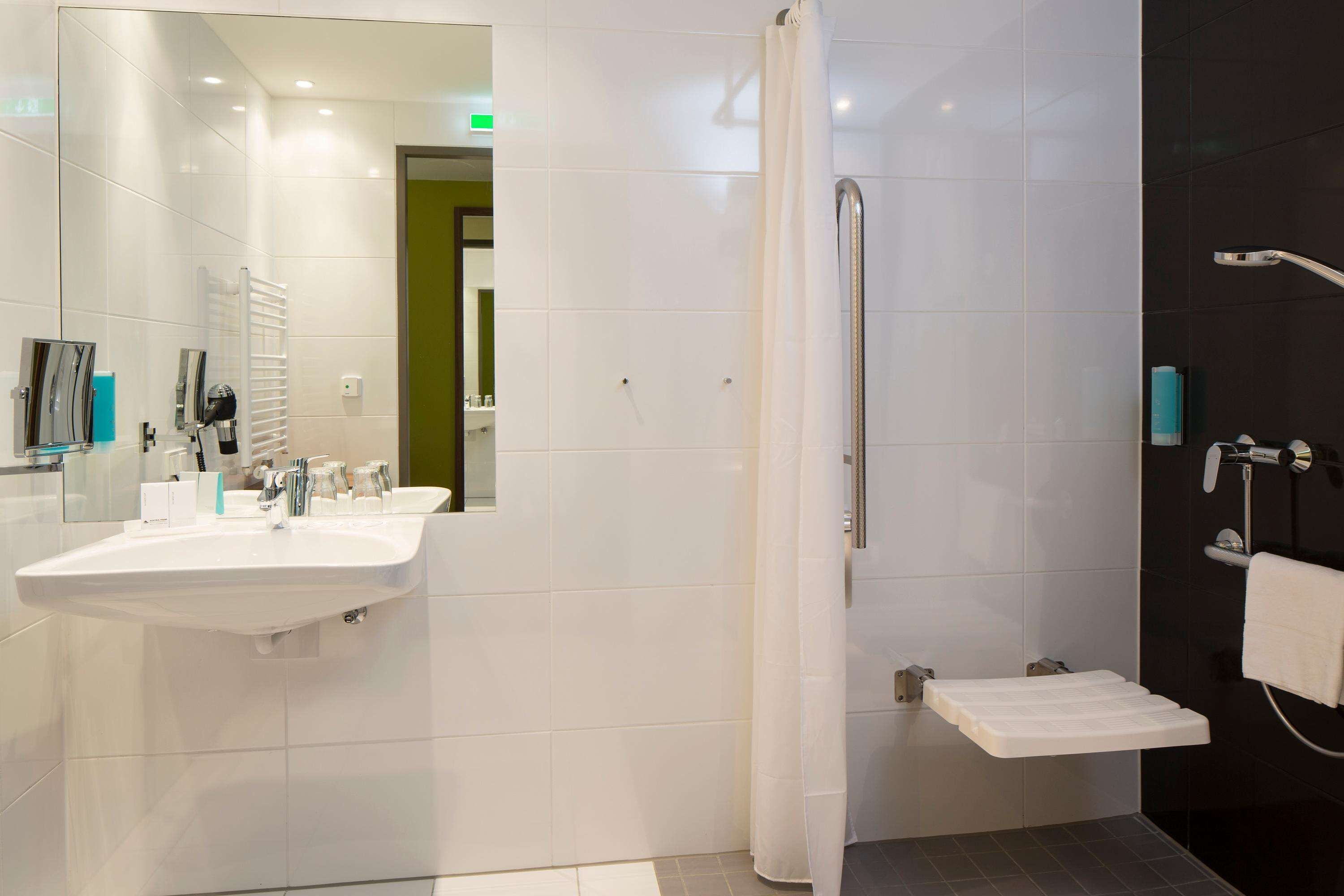 Un baño moderno con lavabo blanco, espejo y zona de ducha.