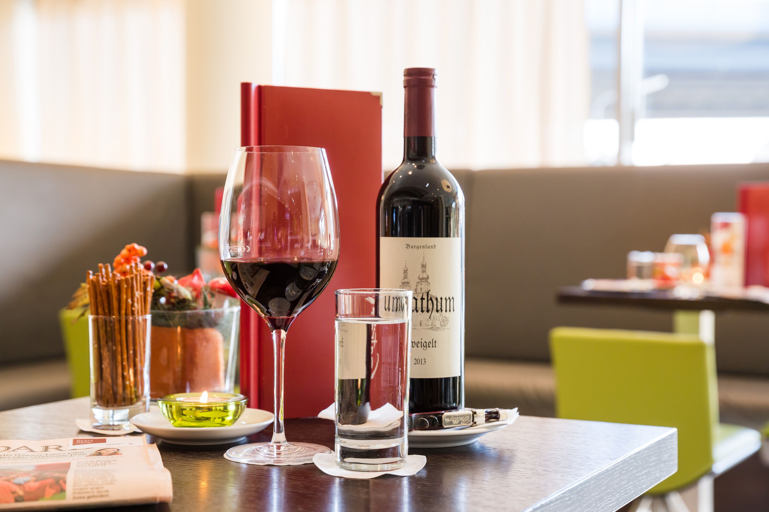 A table with a bottle of wine, a glass of red wine, a glass of water, and a menu.