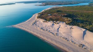 An aerial view of a coastal area with a sandy beach, a small settlement with houses, and a large body of water. - The Berkeley River Lodge (Oombulgurri)