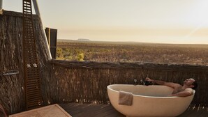 A man relaxing in a large bathtub on a wooden deck with a view of a forested landscape. - The Berkeley River Lodge (Oombulgurri)
