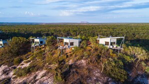 Three modern cabins with external staircases, surrounded by dense bushland and a distant mountain. - The Berkeley River Lodge (Oombulgurri)