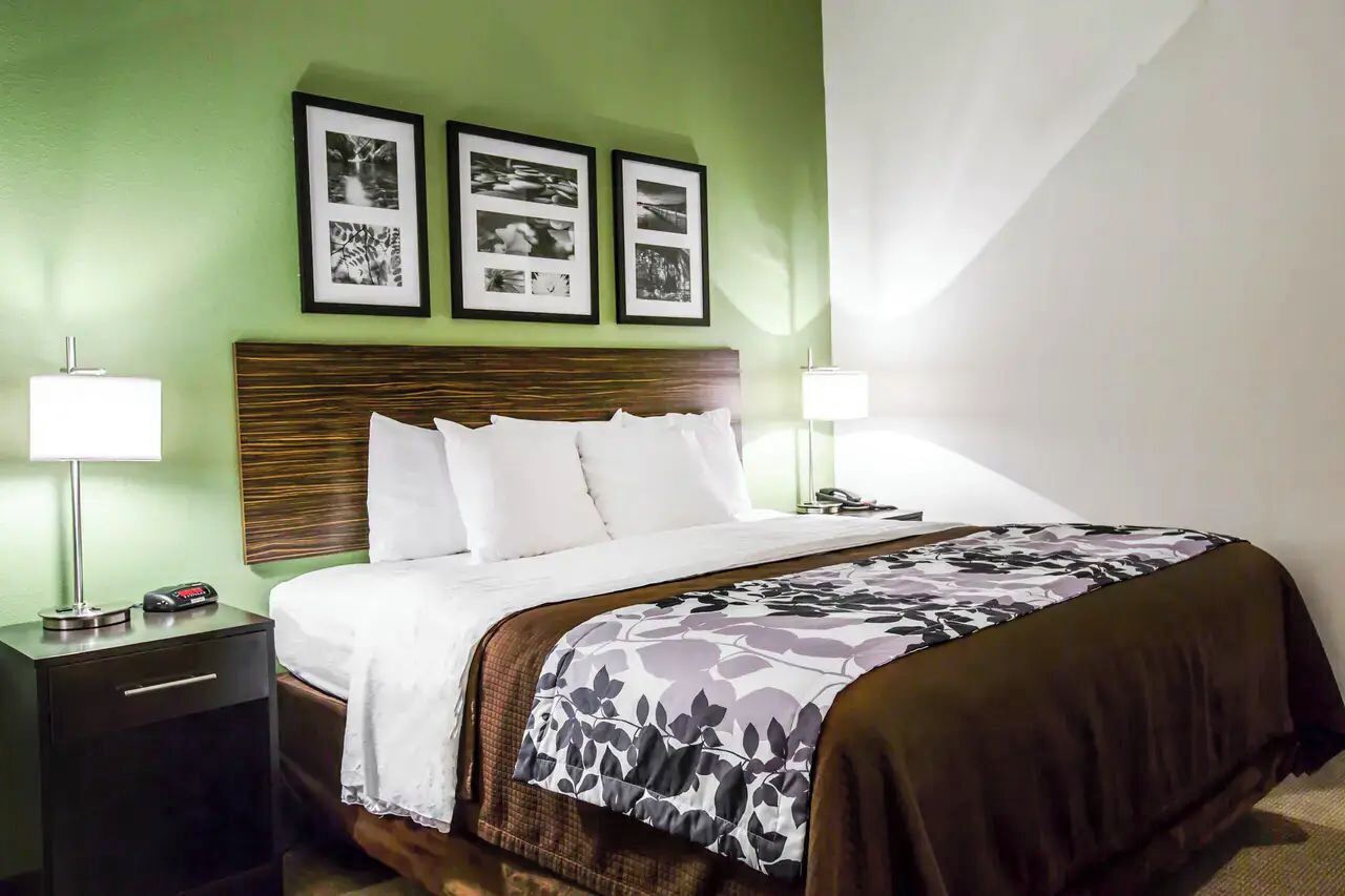 Una habitación de hotel con una cama, dos mesitas de noche, una cabecera y cuadros en la pared.