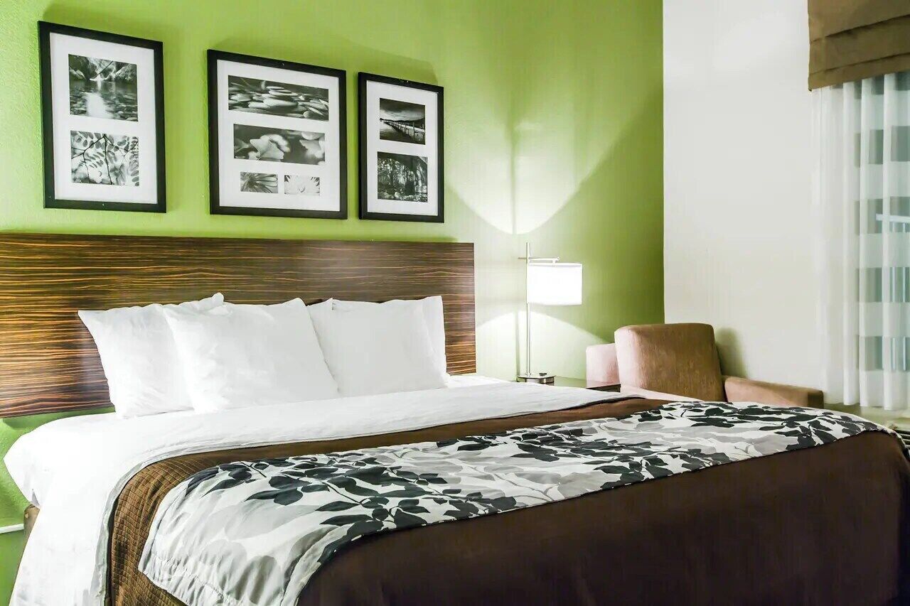 A hotel room with a bed, a headboard, a chair, and framed pictures on the wall.
