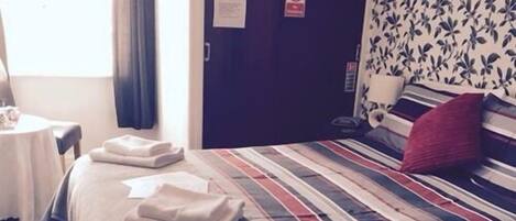 A hotel room with a bed, a table with towels, a window with curtains, and a door with a sign.