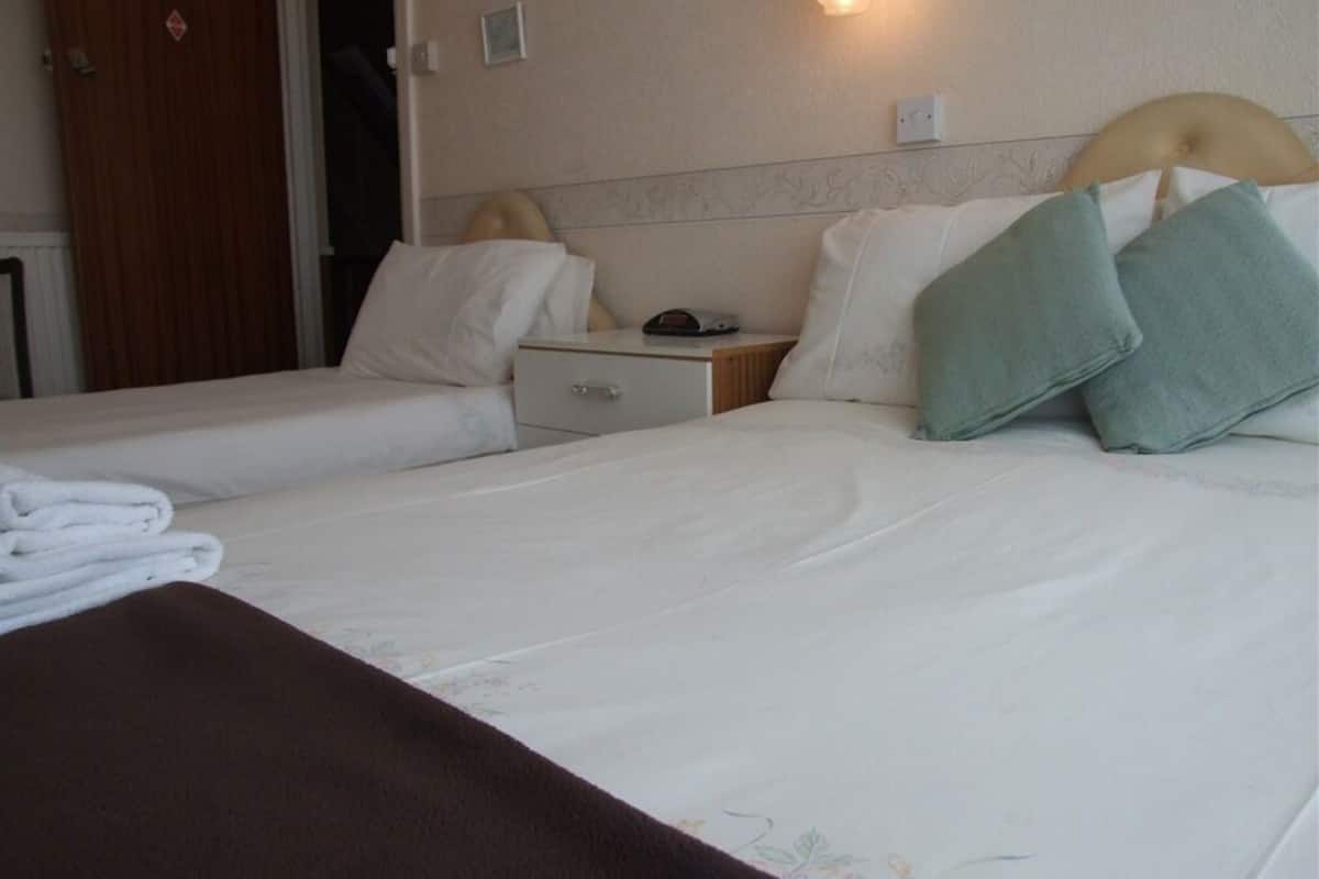 A hotel room with two single beds, a wooden wardrobe, a bedside table with a lamp, and a wall-mounted light.