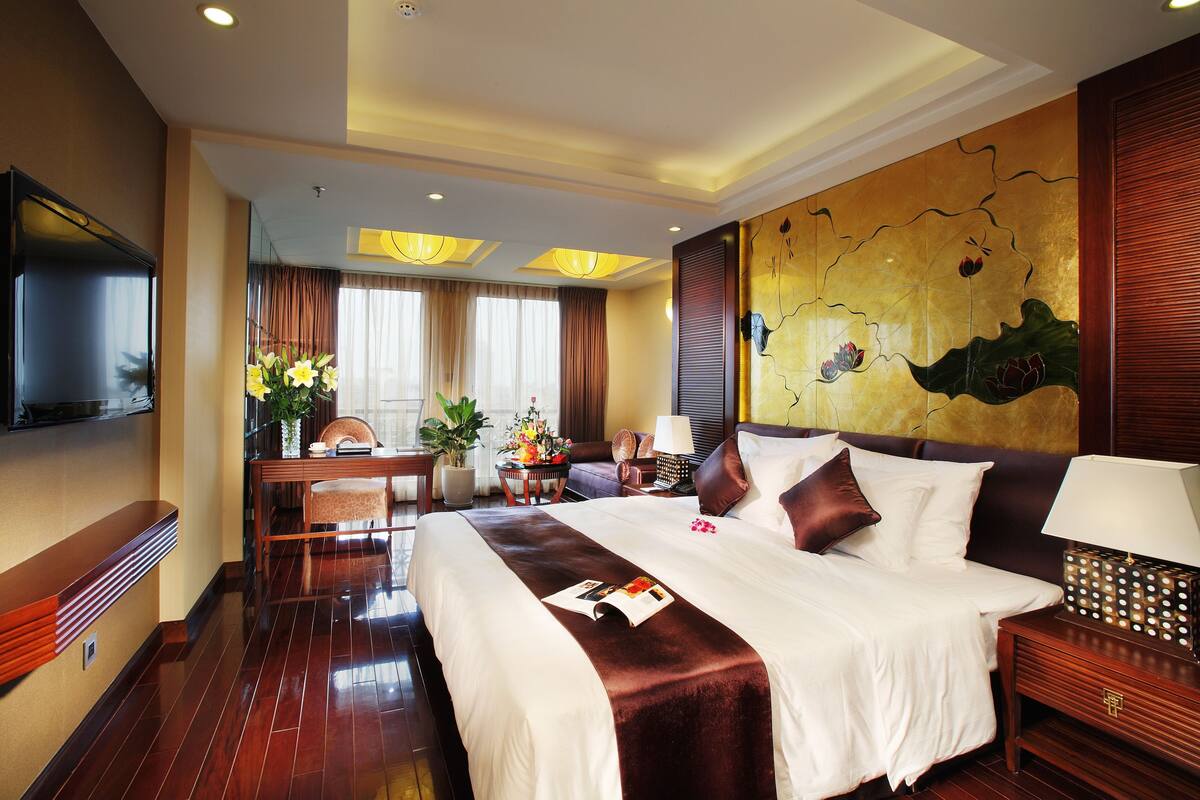 Une chambre d’hôtel avec un grand lit, une télévision, un coin repas avec une table et des chaises, et un mur décoratif.