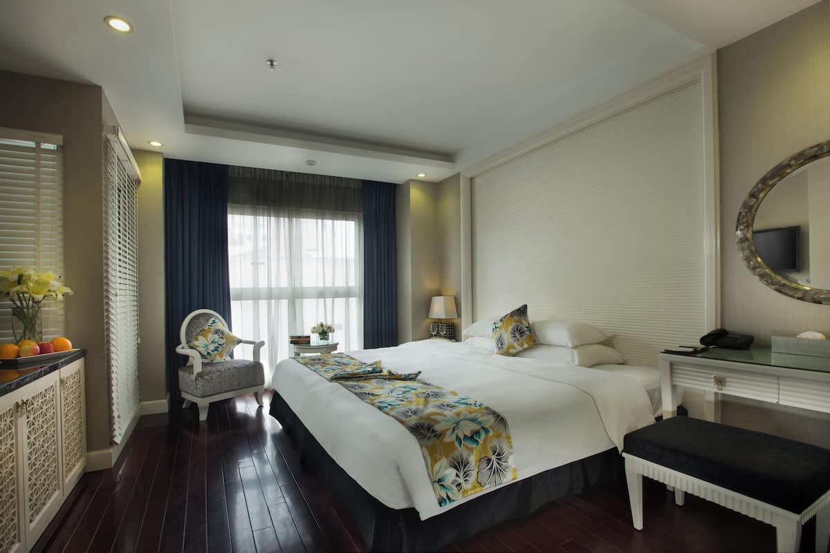 Une chambre d’hôtel avec un grand lit, une table de chevet, une chaise, un bureau et un miroir.