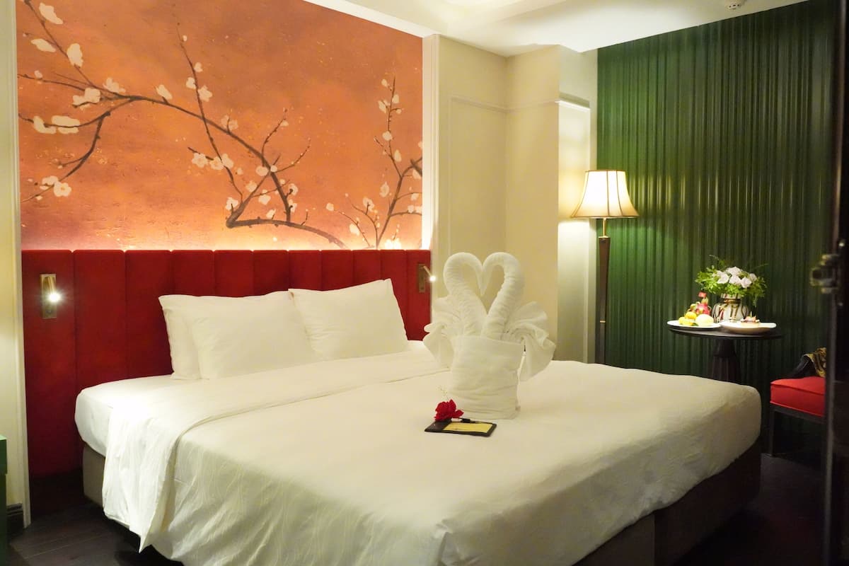 Une chambre d’hôtel avec un grand lit, un mur d’accent rouge, un mur d’accent vert, une table ronde avec une lampe et une petite plante.