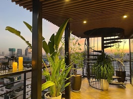 A rooftop terrace with potted plants, a spiral staircase, and a city skyline view.