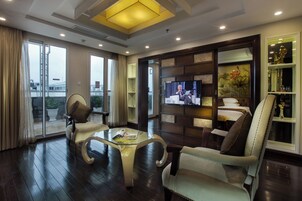 A modern living room with a glass coffee table, leather armchairs, a television, and a bookshelf.
