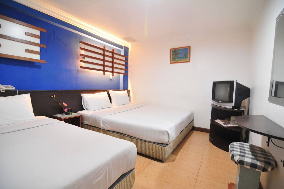 Ein Hotelzimmer mit zwei Betten, einem Fernseher, einem kleinen Tisch und einer Bank.