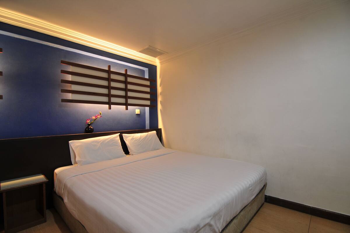 Ein Hotelzimmer mit einem großen Bett, einem Nachttisch, einer Wandleuchte und einer dekorativen Vasen mit Blumen.