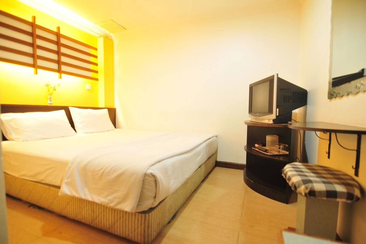 Ein Hotelzimmer mit einem Bett, einem Fernseher auf einem Tisch, einem kleinen Beistelltisch und einer Bank.