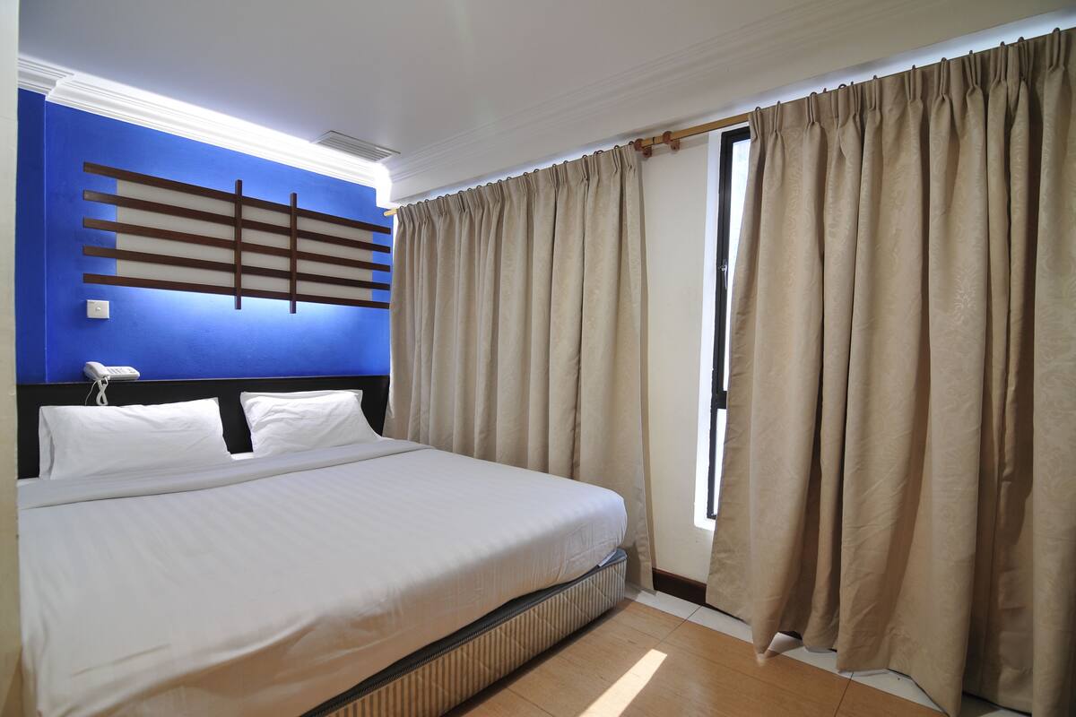 Ein Hotelzimmer mit einem großen Bett, beigen Vorhängen, einer blauen Akzentwand und einem fenster mit Vorhängen.