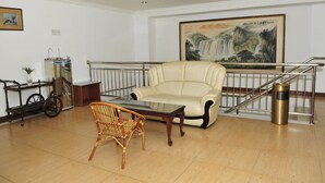 Un hall d’entrée avec un canapé, un fauteuil en osier, une petite table, un chariot sur lequel est posé un vélo, et un tableau accroché au mur.