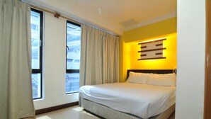 Une chambre d’hôtel avec un lit, des rideaux, une fenêtre et un luminaire fixé au mur.
