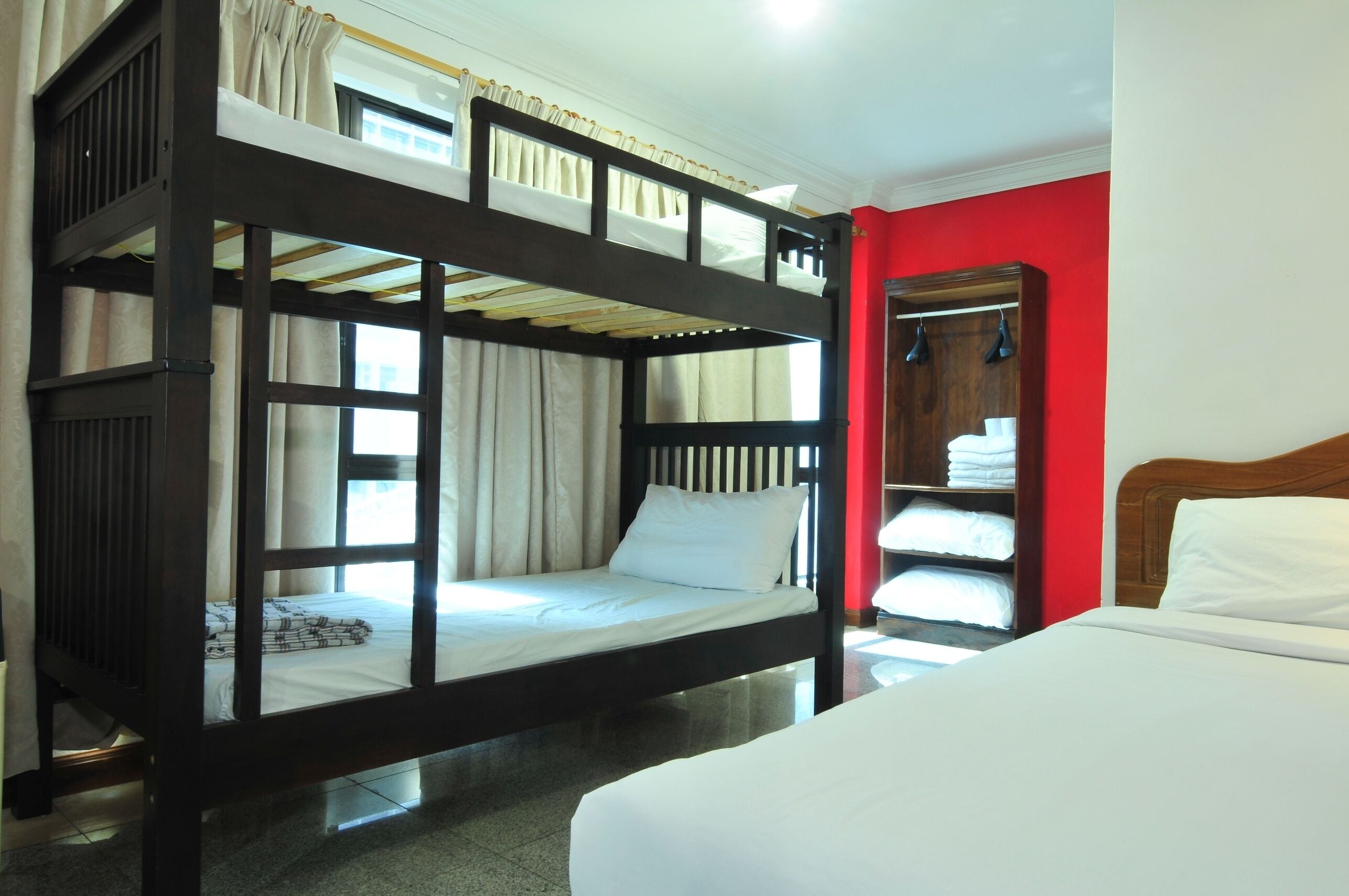 A bunk bed room with a red wall, a wooden headboard, and a white bed.