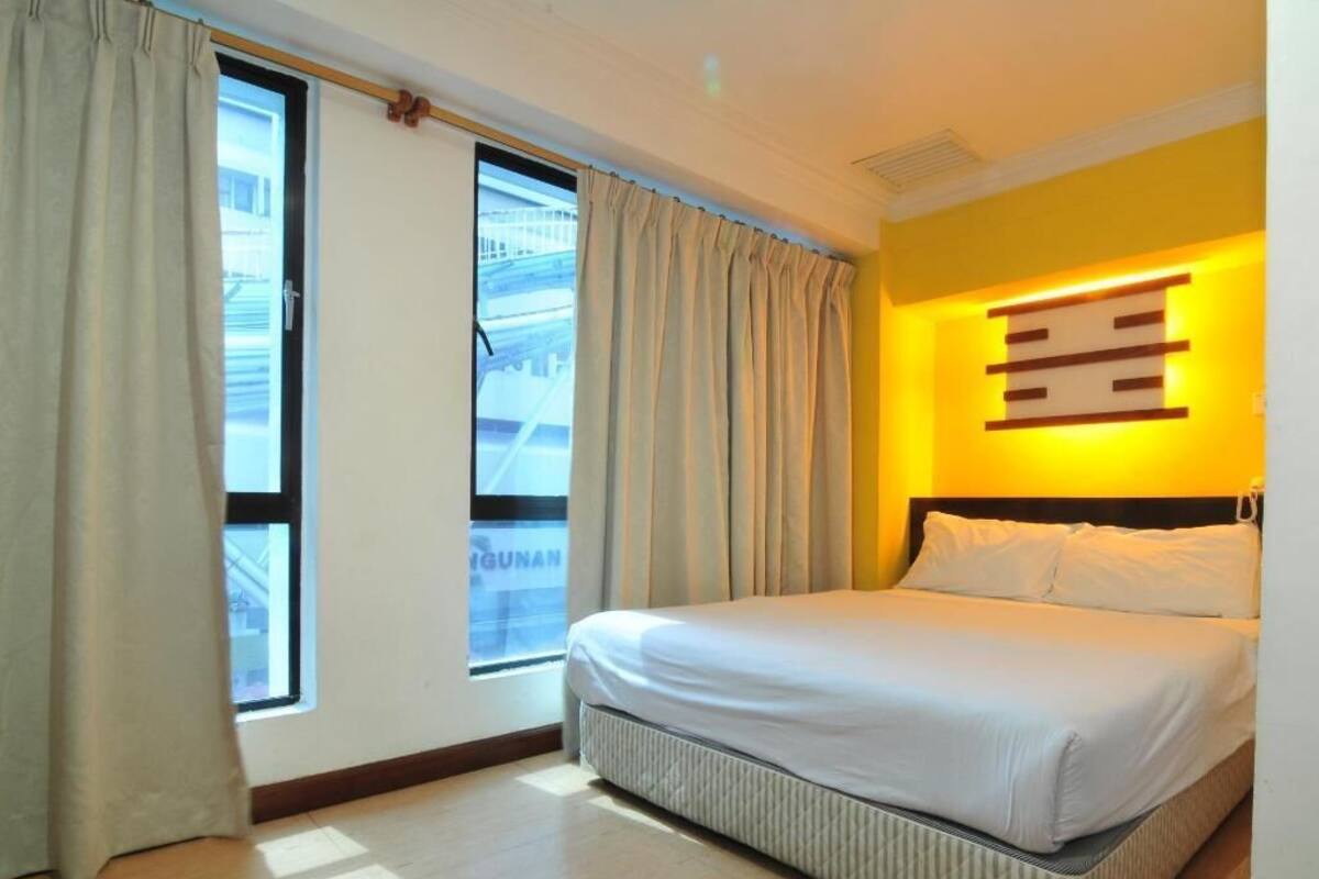 Ein Hotelzimmer mit Bett, Vorhängen, einem Fenster mit Blick und einer Wandleuchte.