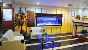 Un hall d’hôtel comprenant un grand aquarium, un présentoir avec une carte, un canapé blanc, une table basse et une plante en pot.