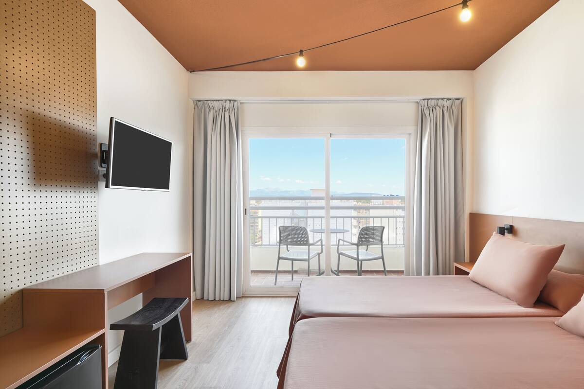 Une chambre d’hôtel avec un lit, un bureau, une télévision et un balcon équipé de chaises.