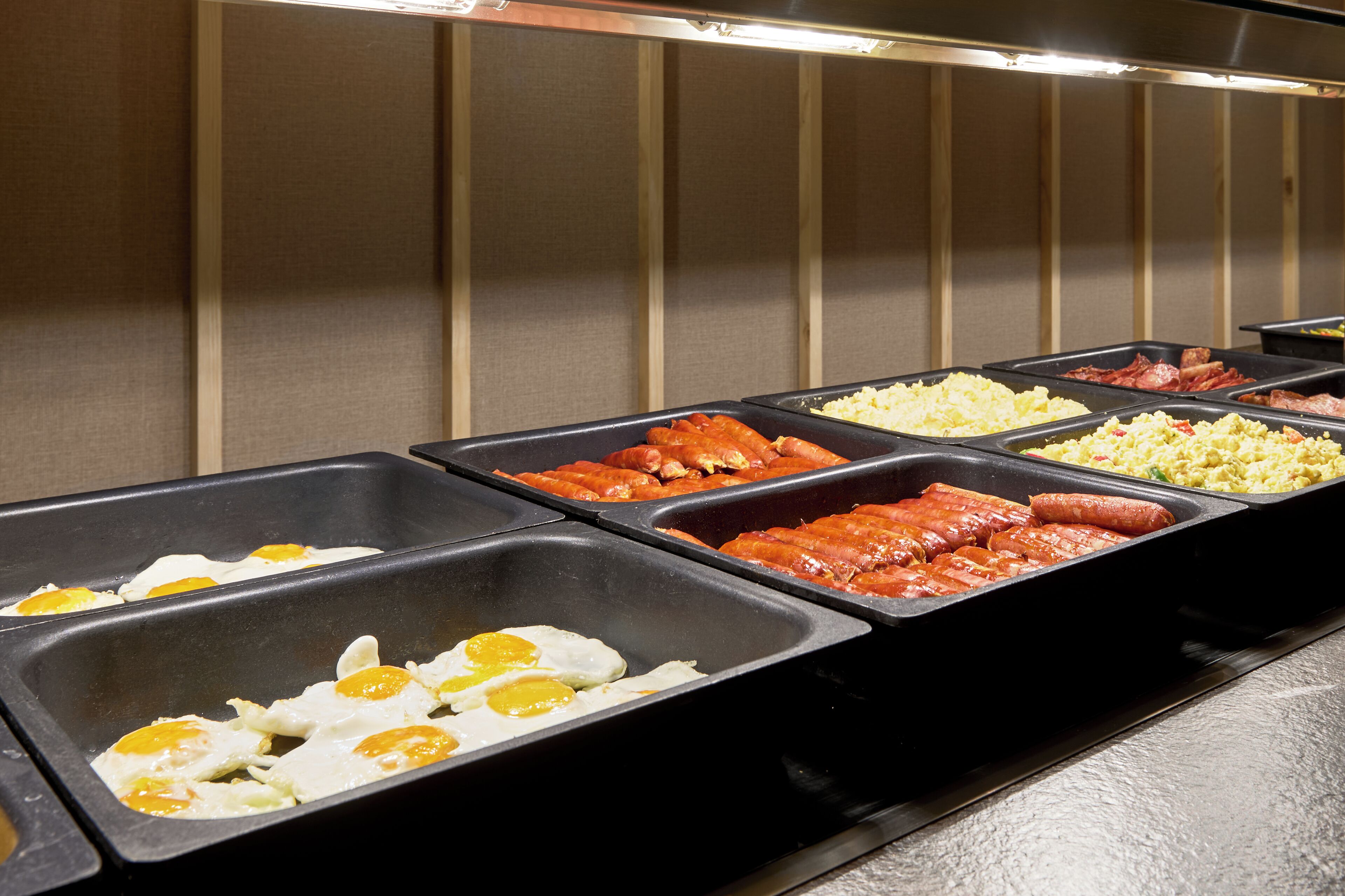 Un bufé con diversas opciones de comida, incluyendo huevos, salchichas y otros platos.