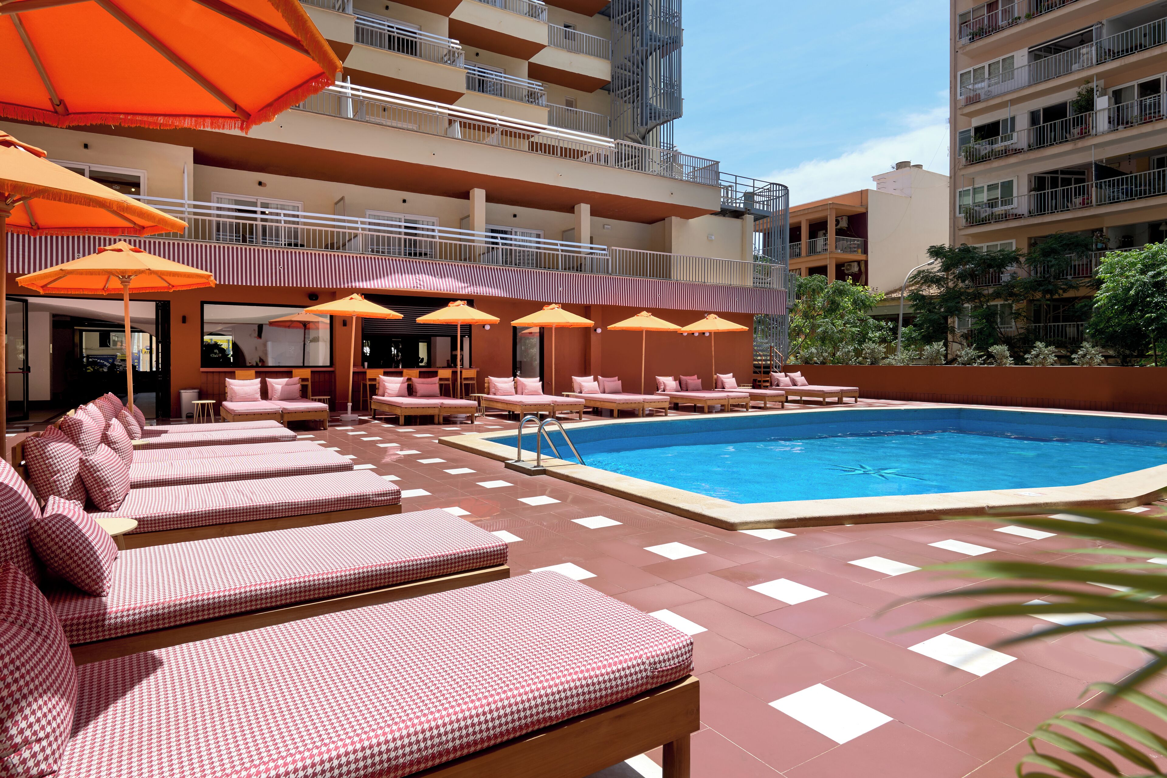 Un área de piscina en la azotea con sillones de descanso y sombrillas, rodeada de edificios altos.
