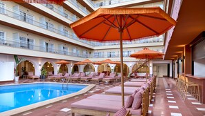 Eine mehrstöckige Hotelhalle mit Schwimmbecken, Liegestühlen und orangefarbenen Sonnenschirmen.