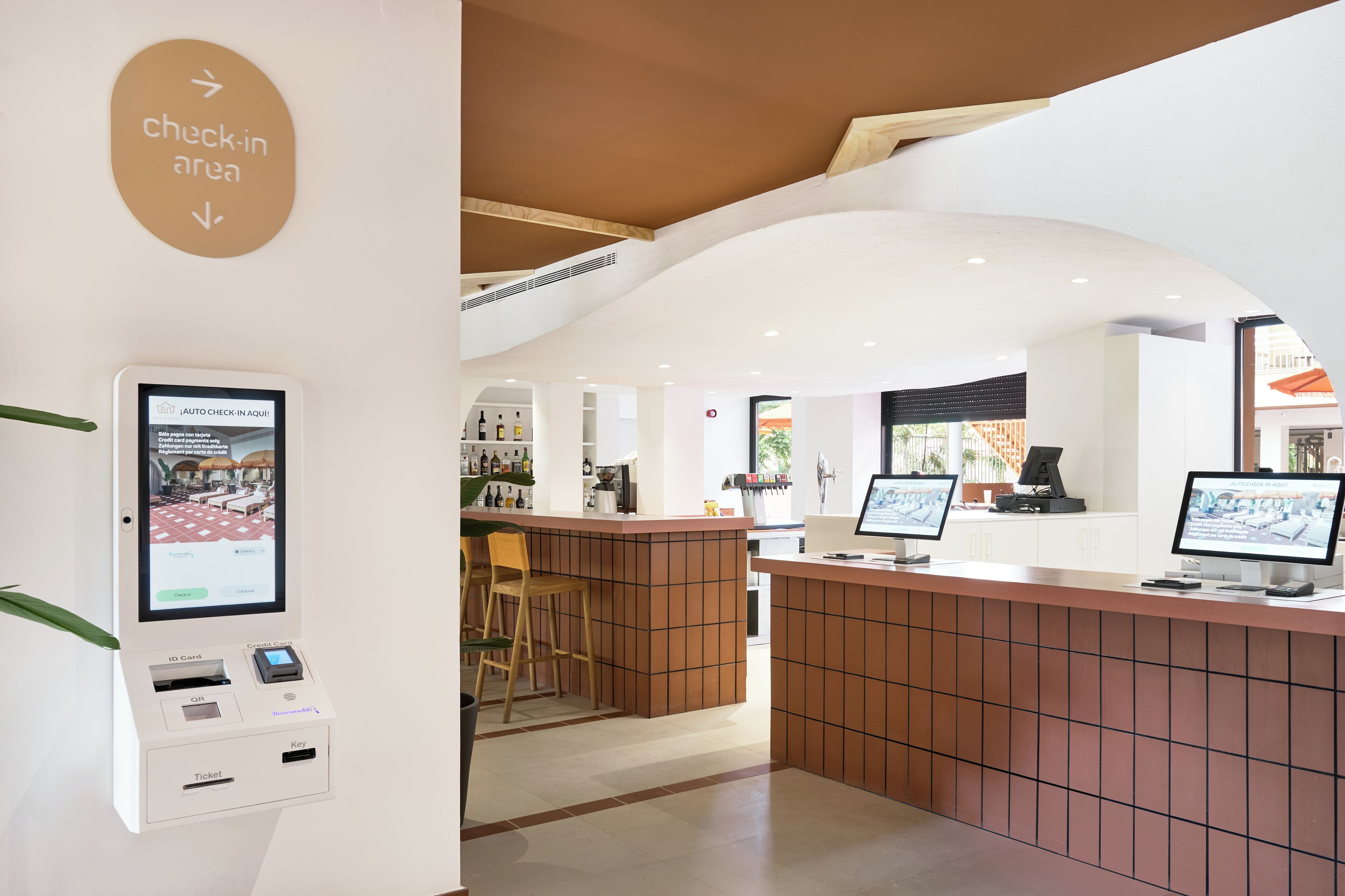 A check-in area with a self-service kiosk, seating area, and a reception desk.