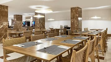 Ein Hotel-Speisesaal mit langen Holztischen, gewobenen Stühlen und moderner Pendelleuchten.