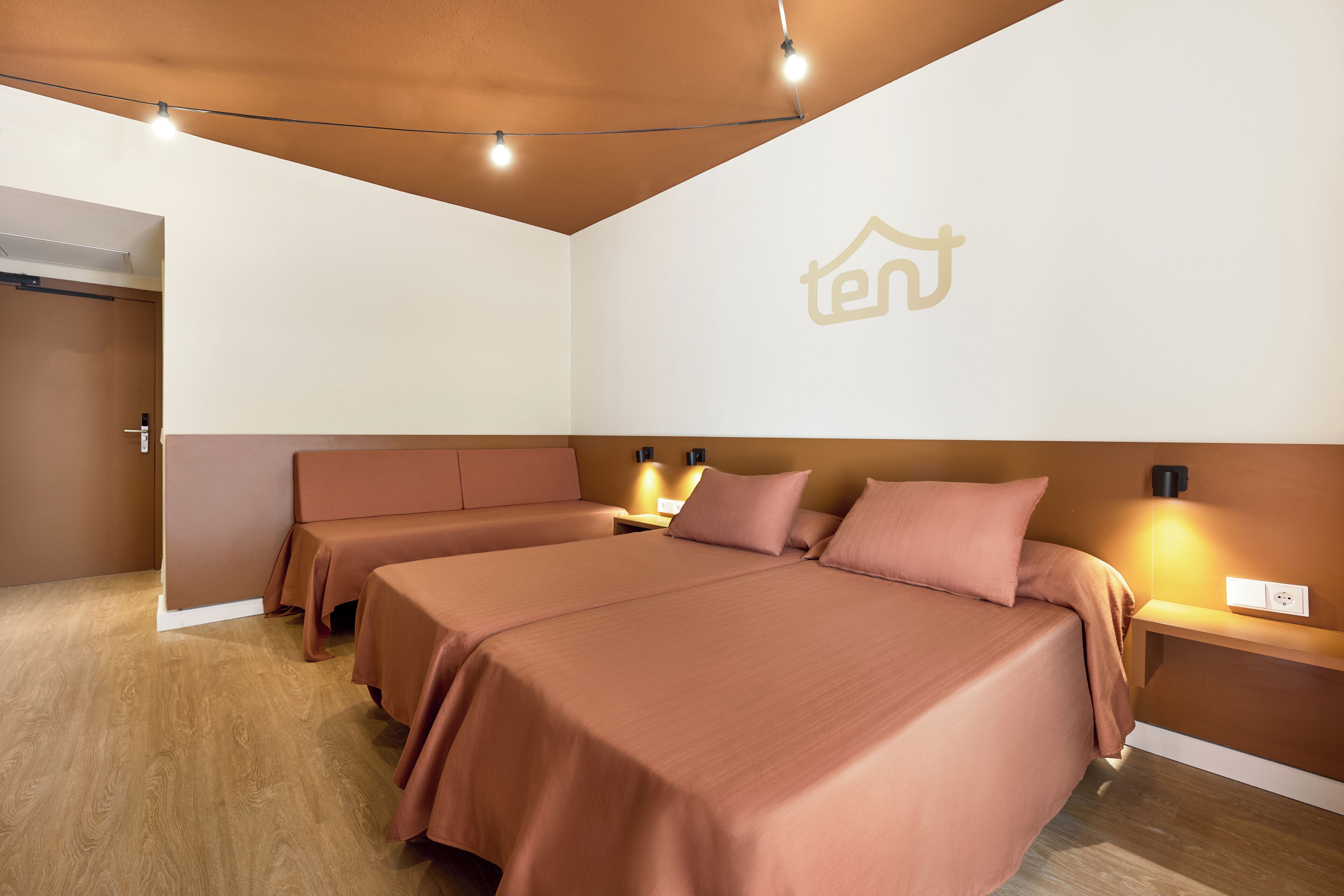 Une chambre d’hôtel avec deux lits, un plancher en bois, un luminaire au plafond et une applique murale.